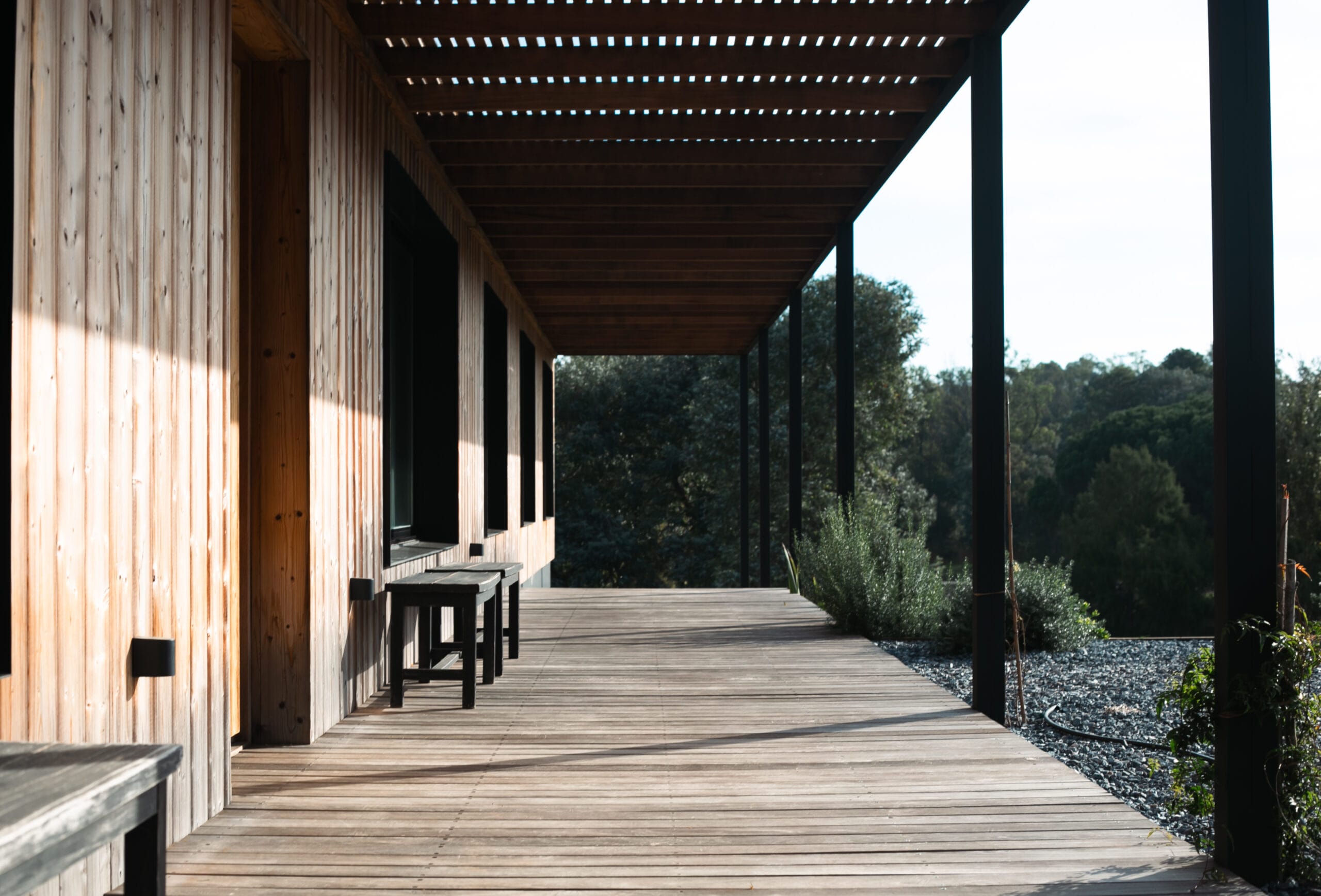 Foto de perspectiva del pasillo lateral, hay un deck y pérgola de madera, y bancos al costado del pasillo.