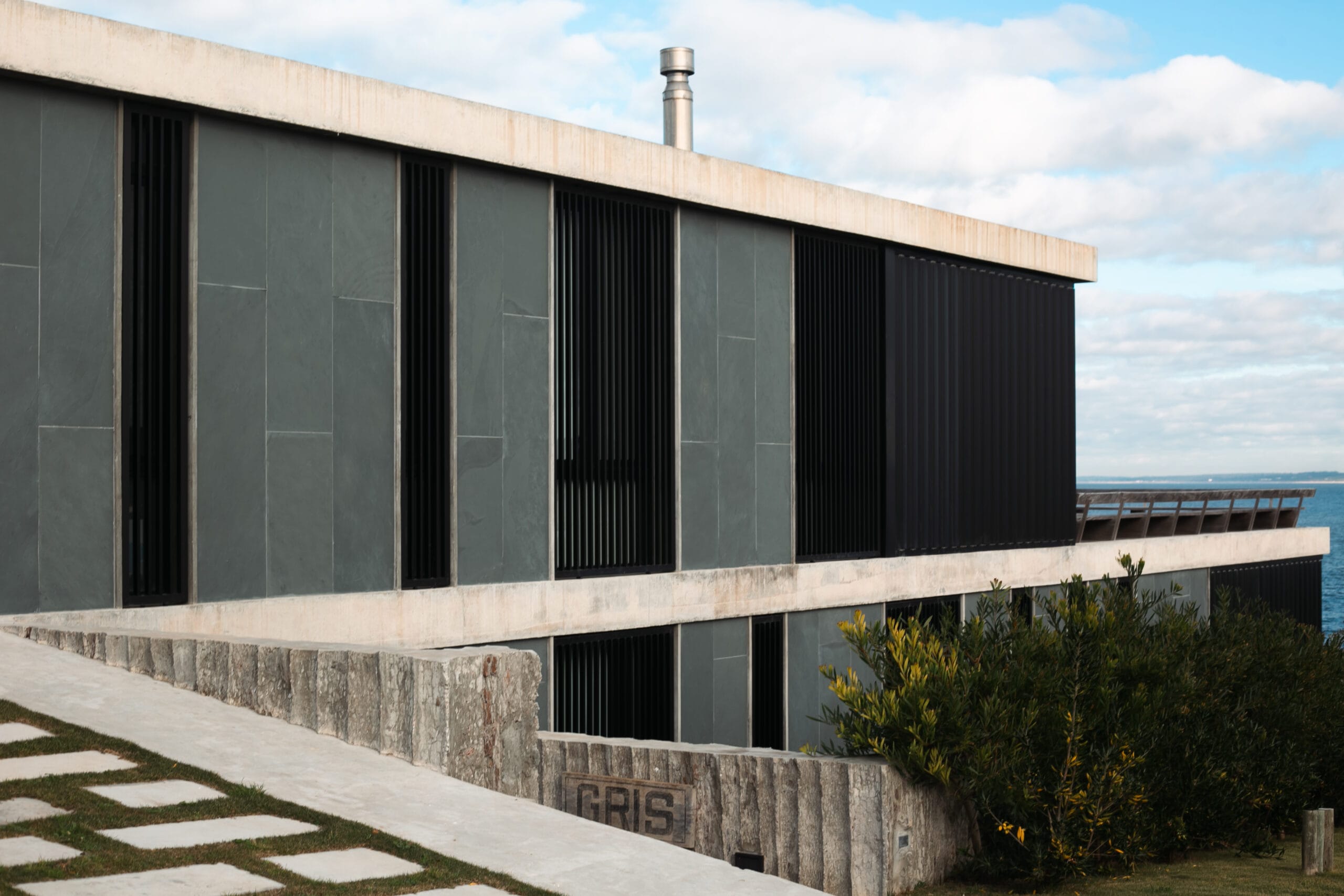 Casa moderna: Gris, frente al mar con una gran ventana lateral, que aporta luminosidad al hogar.