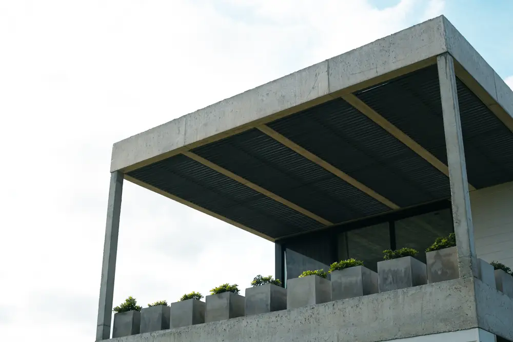 Balcon de piso 2 de Benu, donde se ven varias macetas de hormigón con plantas y una pérgola de madera