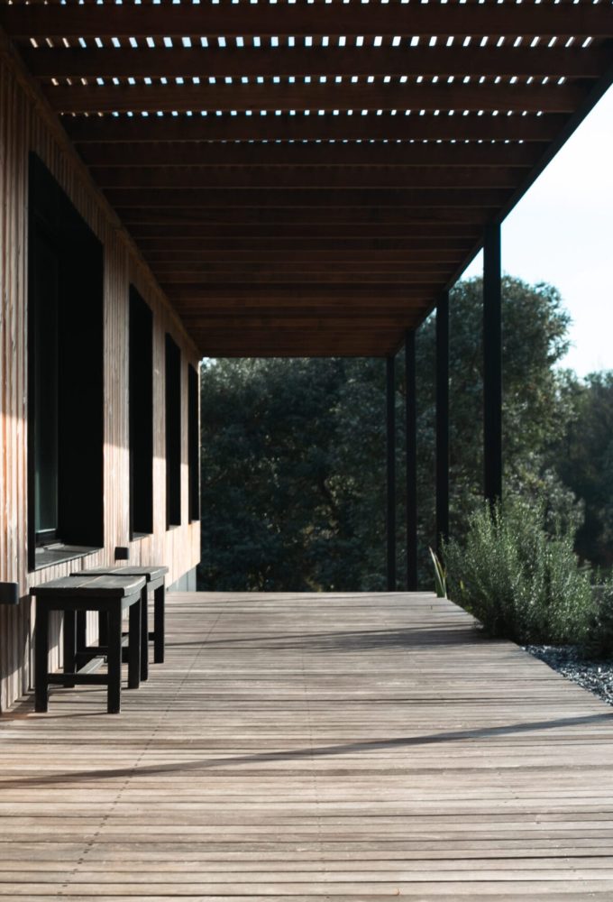 Foto de perspectiva del pasillo lateral, hay un deck y pérgola de madera, y bancos al costado del pasillo.